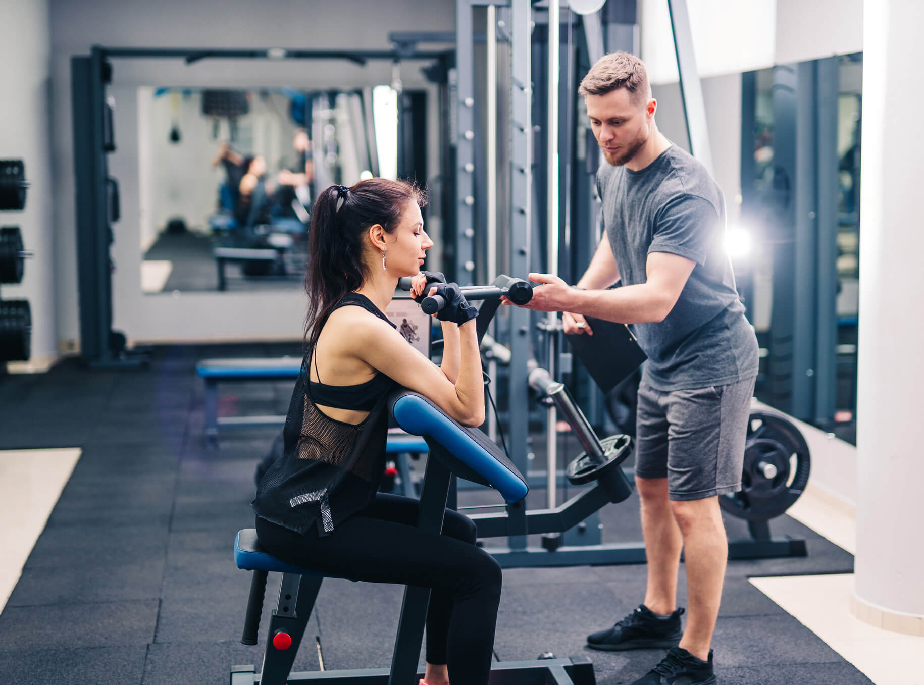 Un personal trainer aiuta una donna a utilizzare un macchinario, regolando i pesi in una palestra moderna.
